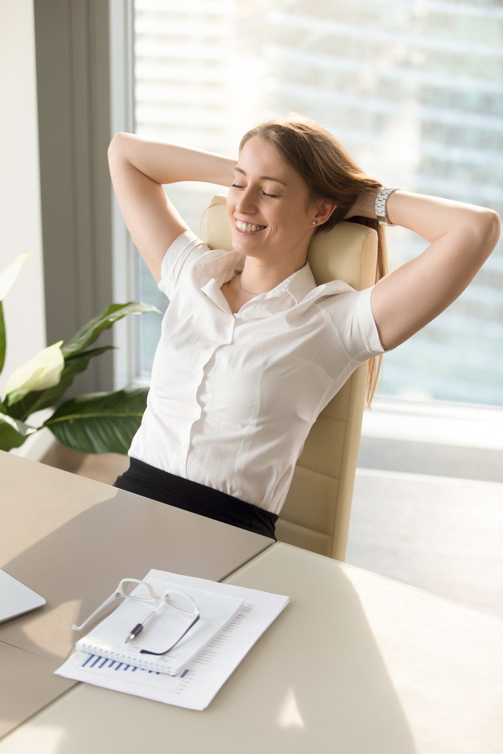 Smiling woman relaxing in office chair, relaxed at work, vertical